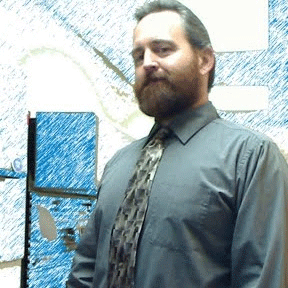 Jayme Johnson, a handsome man of pale complexion and a beard, wearing a green button-up shirt with tie.
