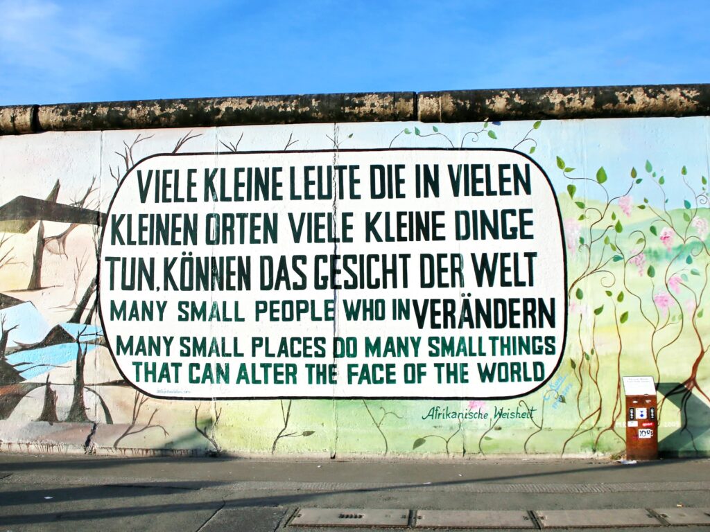 Mural on a wall reads in two languages: Many small people who in many small places do many small things that can alter the face of the world.