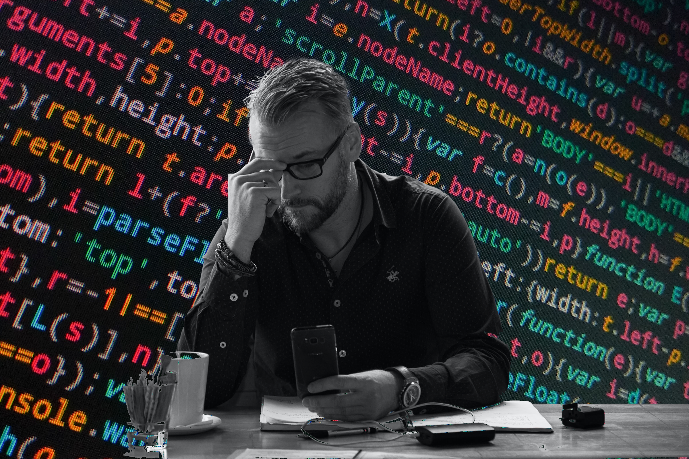 man at desk reviews information in front of a wall of multi-color code